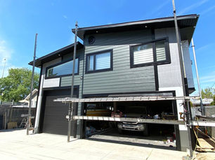 Modern two-story house, dark siding, large windows, scaffolding, under construction.