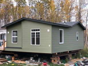 Green modular house elevated on blocks with fall foliage background.