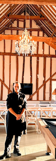 Chef Gerda on location setting up a rustic dining table inside a beautiful timber-framed venue, preparing for a private event with elegant tableware and warm lighting.