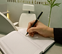 Mão escrevendo em um caderno em um ambiente de coworking da GOD'INS, com o logo "Saúde, Estética & Coworking" ao fundo.