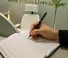 Mão escrevendo em um caderno em um ambiente de coworking da GOD'INS, com o logo "Saúde, Estética & Coworking" ao fundo.