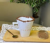 "Caneca Godins branca com borda de chocolate, colher e biscoitos em uma bandeja de madeira."