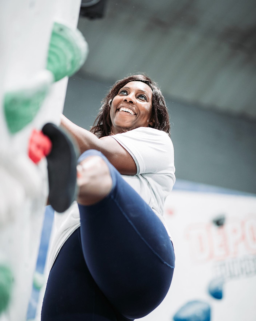 Black female climber, Kumbi Kariwo, bouldering at an indoor climbing wall.