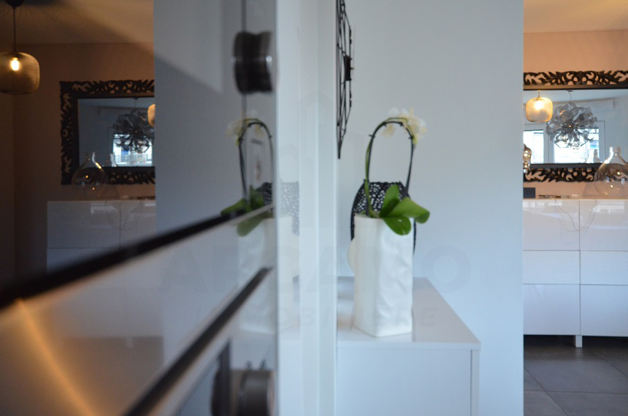 View through a modern apartment interior with white walls, decorative mirrors, pendant lights, a white console, and an orchid.