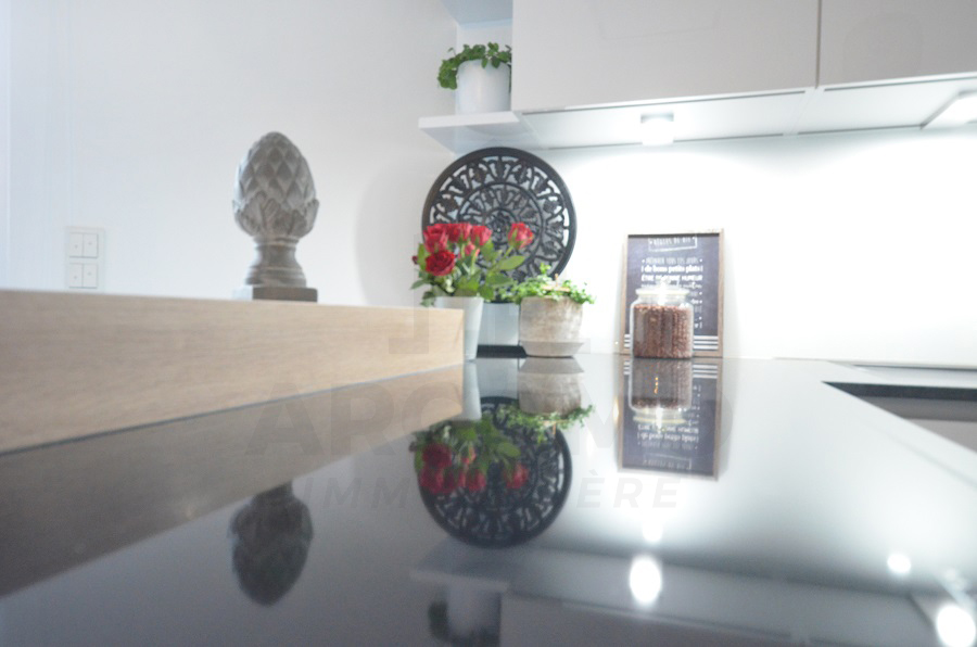 Close view of a glossy black kitchen worktop with decorative plants, flowers, a clock, and a small recipe display.