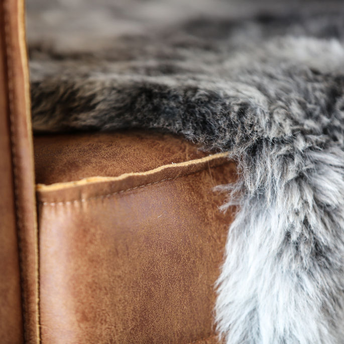 Détail d’un fauteuil en cuir avec peau lainée dans un restaurant en Savoie, mettant en valeur les matières naturelles dans un design d’intérieur chaleureux.