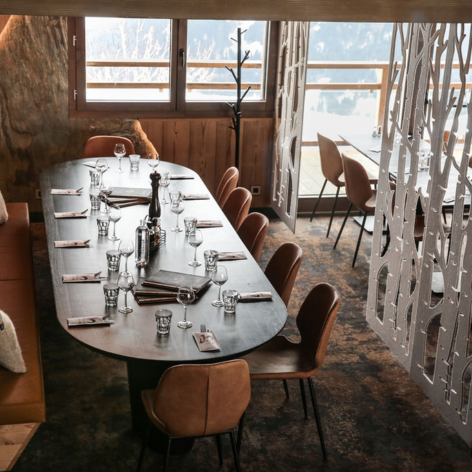 Salle de restaurant en Savoie avec grande table, banquette en cuir et séparation décorative en design d’intérieur contemporain.