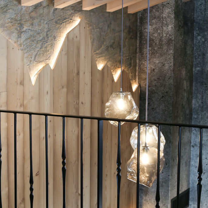 Suspension lumineuse en verre dans un restaurant en Savoie, reliant une mezzanine à la salle principale, avec garde-corps en métal réalisé par un artisan local.