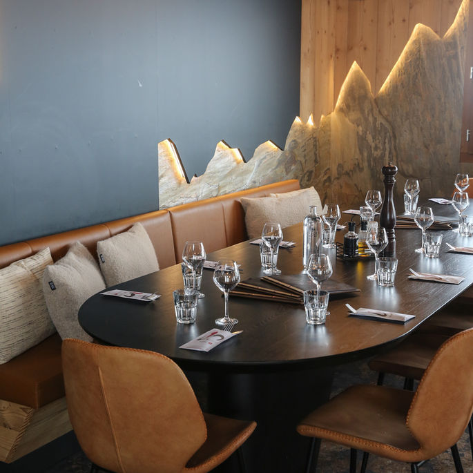 Design d’intérieur d’une grande table conviviale dans un restaurant en Savoie, avec banquette en cuir, bois naturel et fresque murale inspirée de la montagne.