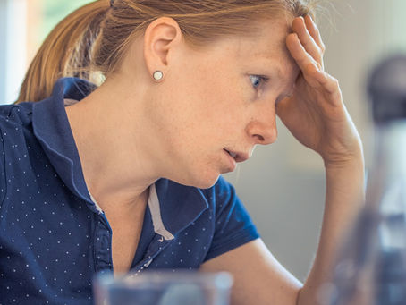 Stressed woman sitting at a laptop with hand on forehead, showing mental exhaustion and the importance of stress management for healthier mind and body.
