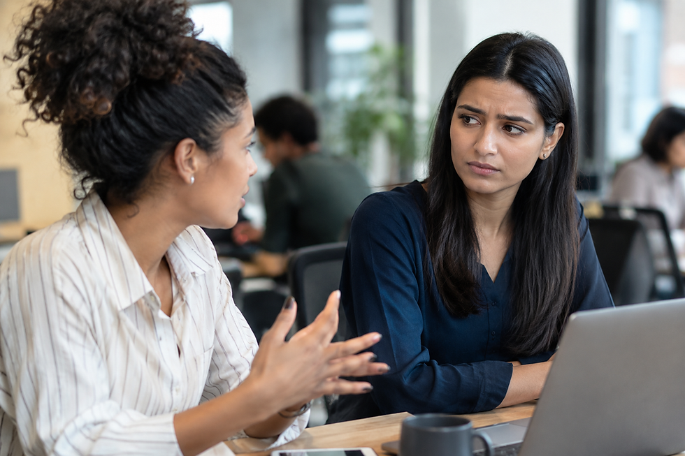 Two diverse coworkers having a conversation as one shows subtle discomfort and hesitation in a modern office