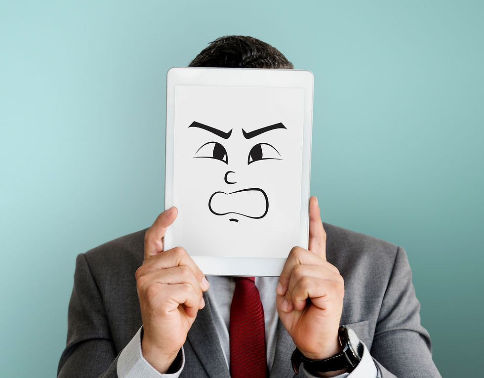 Businessman holding a tablet with a cartoon angry face illustration covering his own face, representing hidden emotions at work.