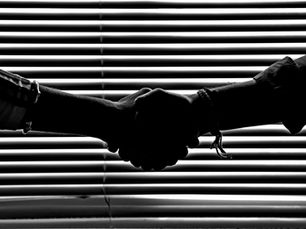 Silhouette of two people shaking hands in front of window blinds
