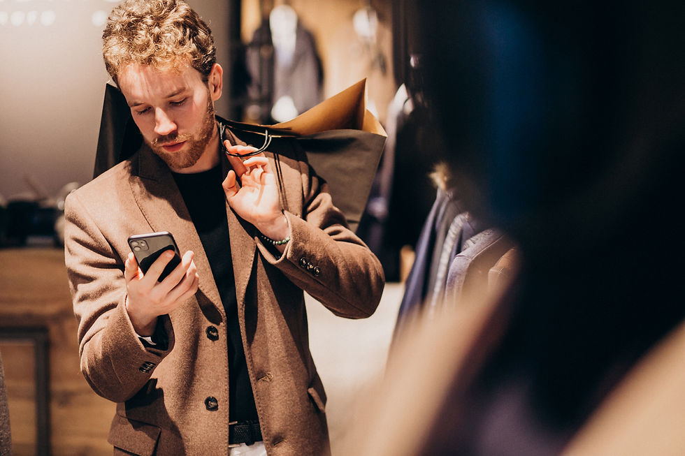 Mobile marketing concept featuring a stylish young man in a menswear shop, carrying shopping bags and using his smartphone, highlighting the influence of mobile devices on luxury retail experiences.