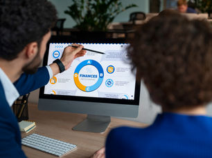 Two professionals in a modern office review a financial infographic on a desktop screen, discussing data integration and cross-departmental metrics—illustrating the collaborative nature of Revenue Operations (RevOps).