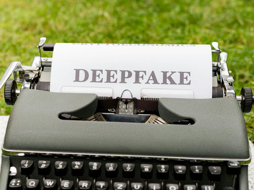 A vintage typewriter with a sheet of paper inserted, displaying the word “DEEPFAKE” in bold letters. The typewriter is set outdoors on a grassy background.