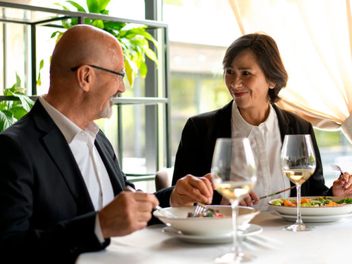 Two business professionals having a relaxed conversation over a meal in an upscale restaurant, illustrating how informal conversations can build trust beyond the boardroom.