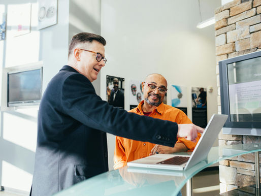 Two businessmen review data on a laptop, discussing market strategy in a modern office.