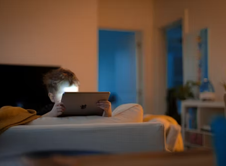 Child using a tablet in a dark room, screen time effects on children.