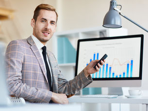 Smiling professional in a modern office presenting data on a large screen—illustrating the evolving role of sales leaders from managing people to designing data-driven systems and scalable processes.