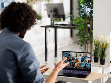 Business professional participating in a virtual meeting with remote team members on a laptop in a bright modern office.