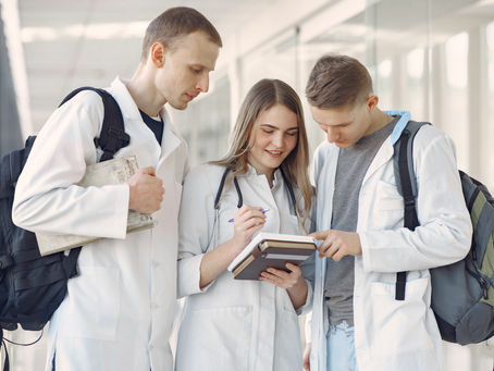 Three medical students in white lab coats reviewing notes together in a university hallway, representing the academic journey from a science diploma to a medical degree.