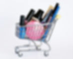 The miniature metal shopping cart is filled to the top with colorful makeup products, creating a playful and aesthetic display often used for beauty marketing or creative flat-lays.