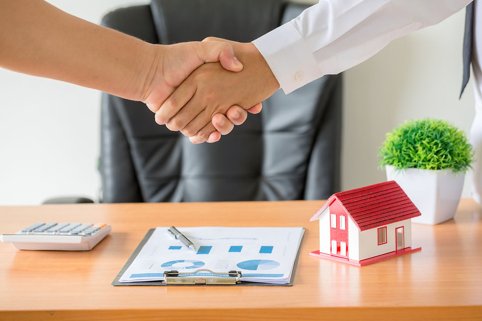 Real estate agent and client shaking hands over a signed property agreement with a house model and financial documents on the desk.