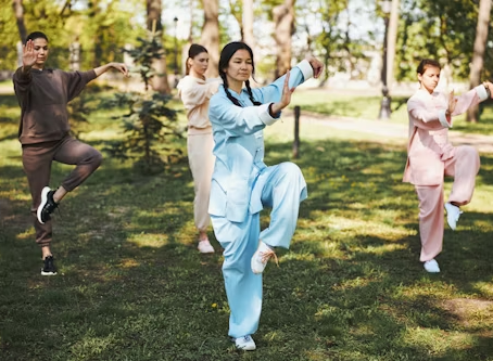 Group of women practicing Tai Chi in a park, wearing traditional clothing and demonstrating poses.