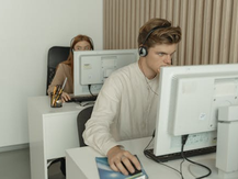 Two office employees working at desktop computers, wearing headsets in a quiet, modern workspace, focused on their screens during customer support or data tasks.