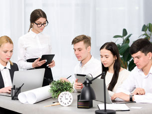 Cross-departmental sales team collaborating at a conference table with laptops and digital tablets, demonstrating effective communication strategies in a modern office setting