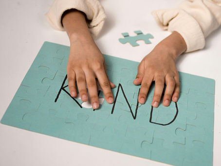 Child's hands on a puzzle that spells "KIND," with a missing piece. 