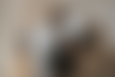 Person working at a minimalist home office desk, seated on a chair, using a desktop computer and laptop with code or documents on the screens.