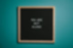 Black letter board with wooden frame on teal background reads, "YOU ARE NOT ALONE," conveying a reassuring message from a perinatal mental health specialist for grieving dads.