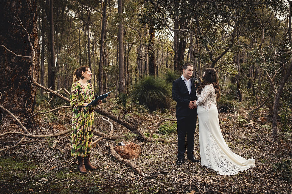 Bride and groom stand hand in hand during an outdoor forest wedding as an officiant reads from a folder.