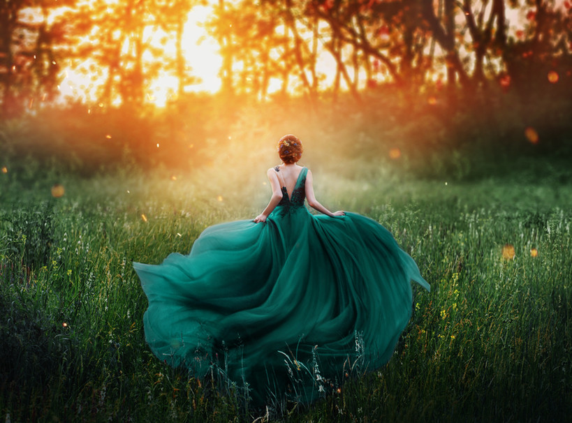 A woman in an emerald gown moving through a sunlit forest