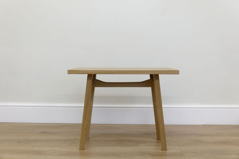 a small wooden table sits on a wooden floor in front of a white wall