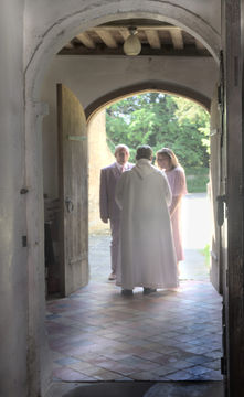 Scene taken from inside the church looking out through the door with the vicar greeting the bride and groom.