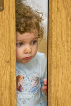 A small child with her nose pressed against a glass window looking to see what is happening