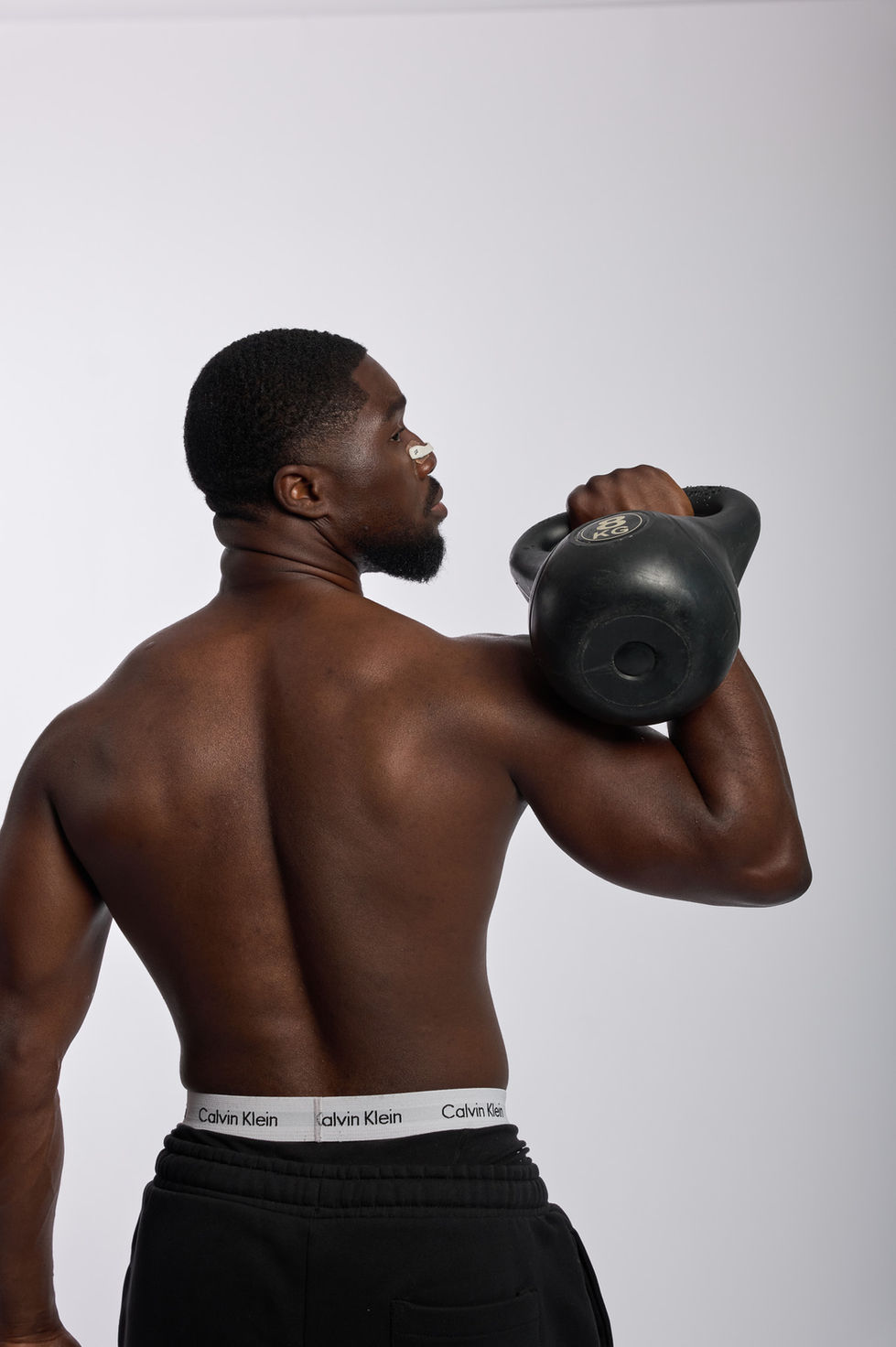 Man holding kettlebell on shoulder, facing away.