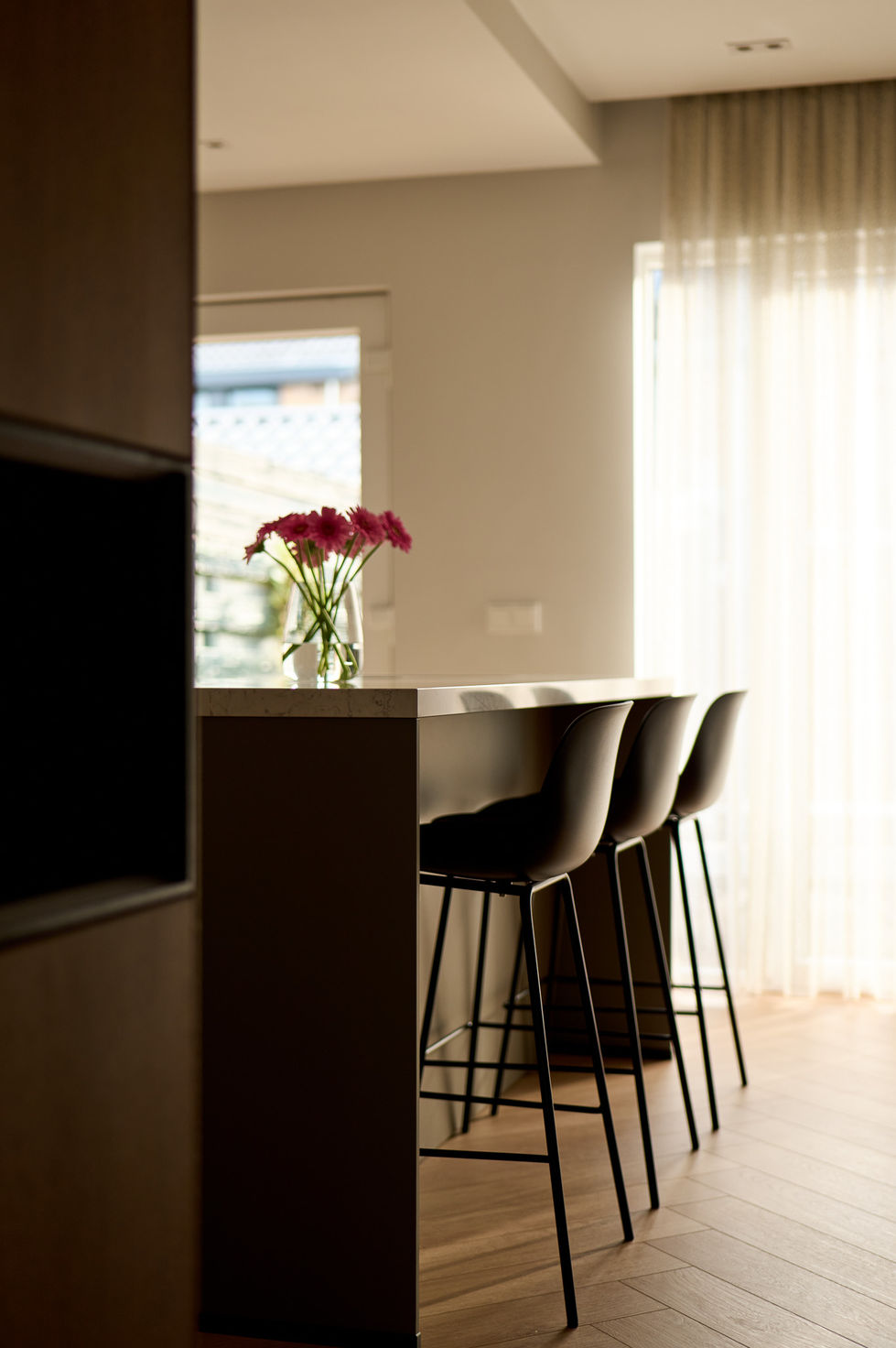 Modern kitchen with bar stools and flowers on counter.
