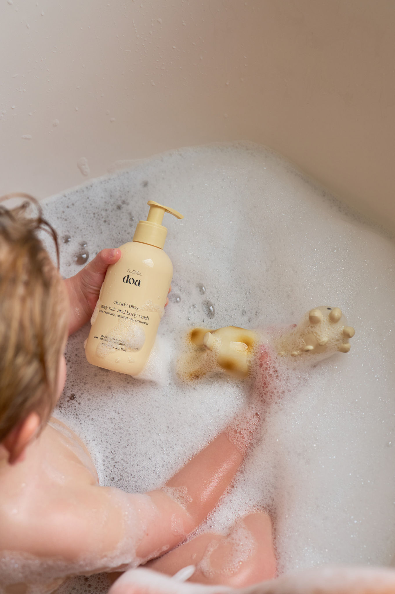 Child in bath holding a bottle of shampoo.