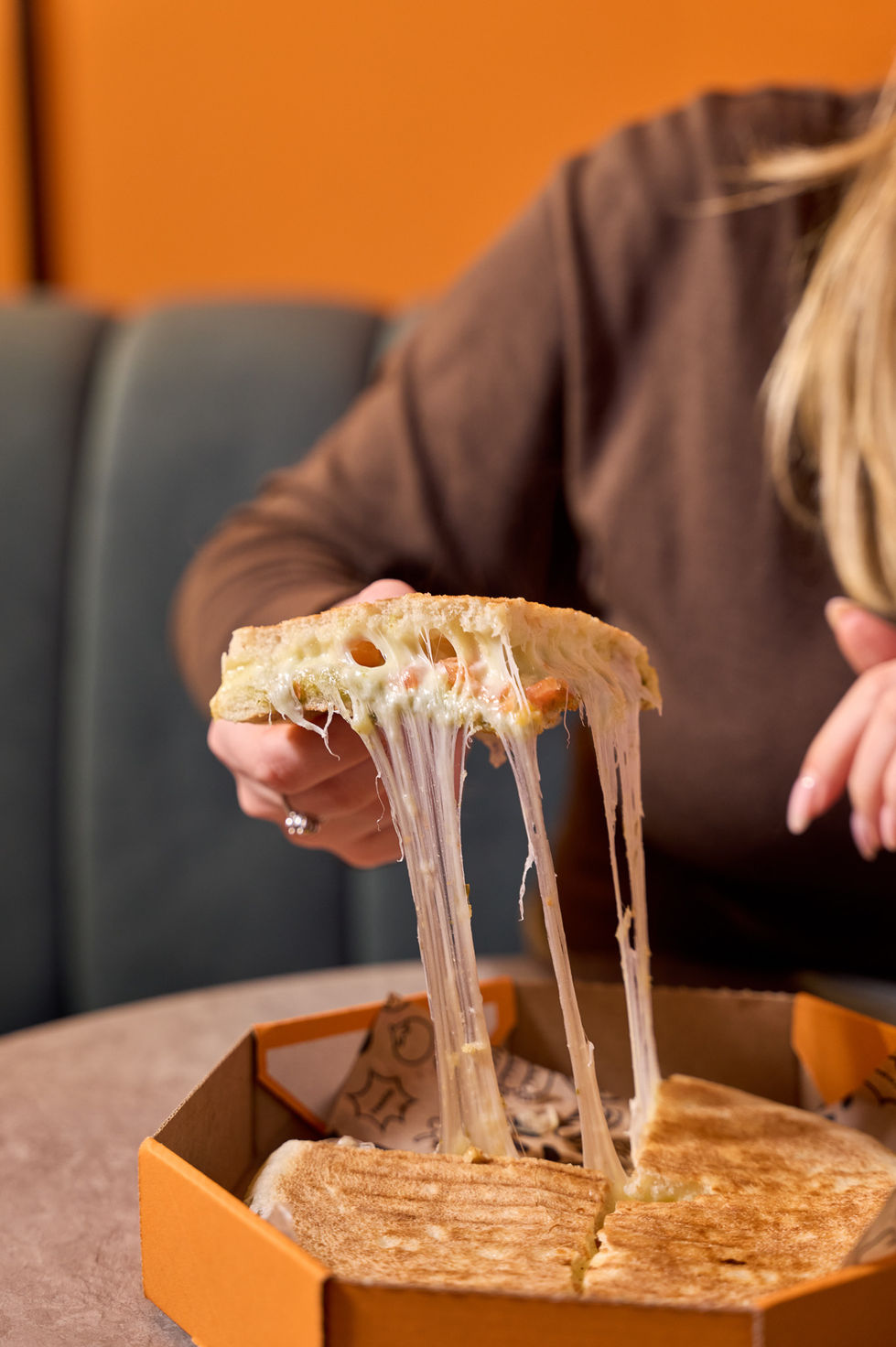 Person pulling cheesy pizza slice with stretchy cheese.