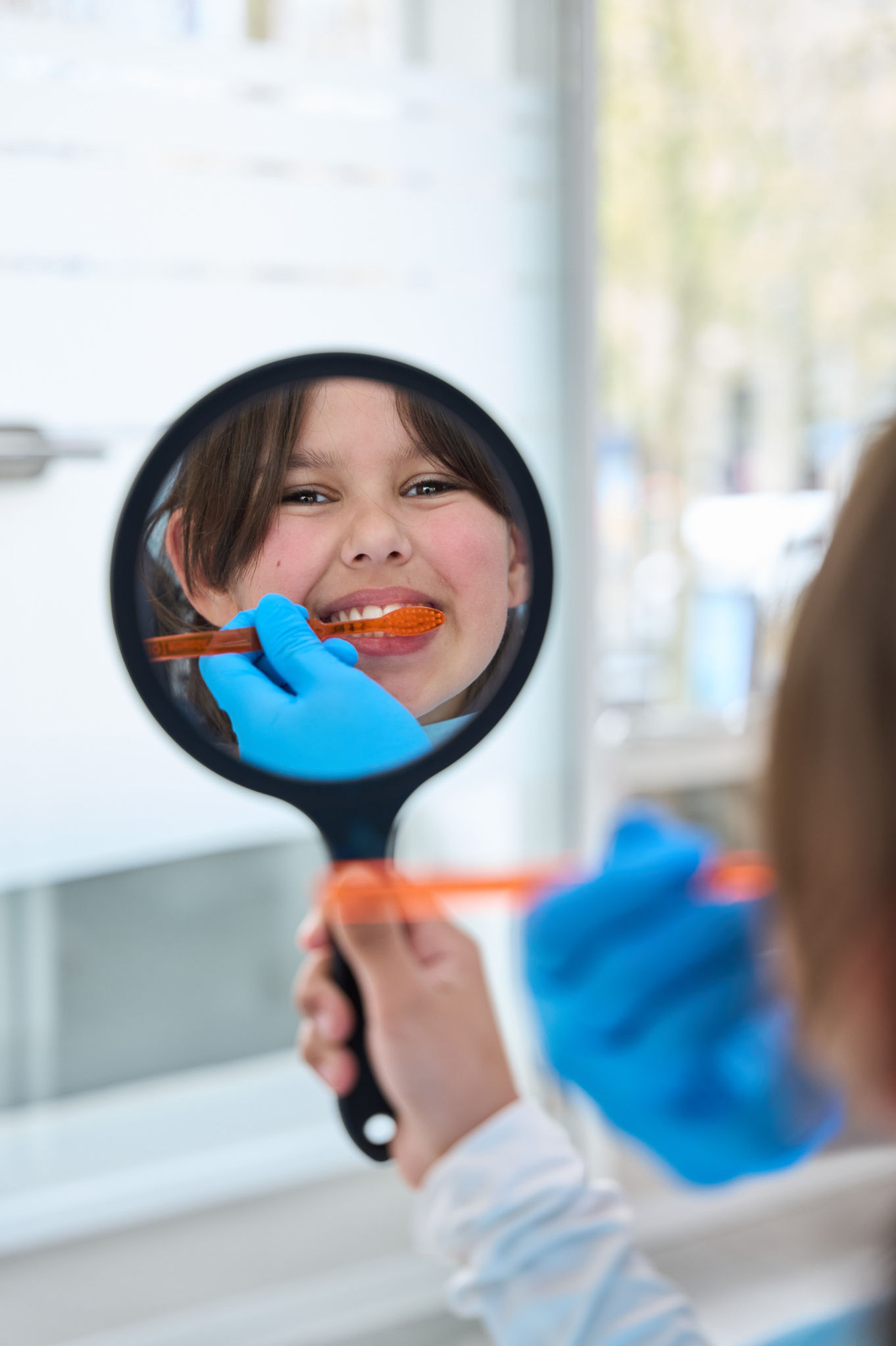 Child brushing teeth, reflected in a hand mirror.