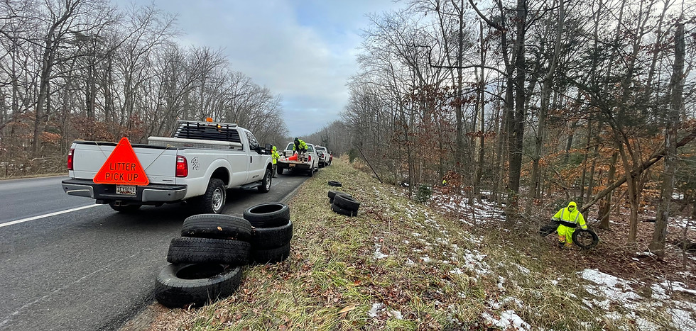 Government roadside cleanup crew removing illegally dumped tires and debris along roadway in Maryland with safety vehicles and signage