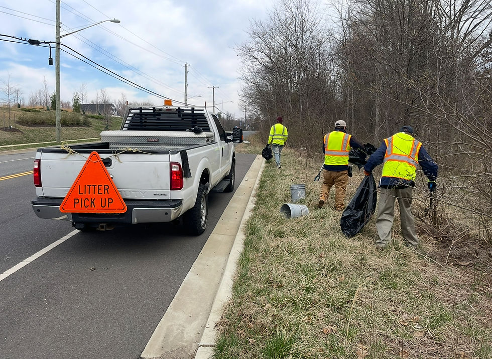 Roadside litter removal crew cleaning debris along a Maryland roadway beside a truck with a litter pick up sign.