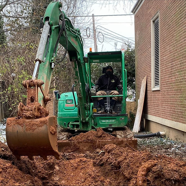 ASAP Waste Services operator using a compact excavator to manage soil and debris removal beside a commercial building, supporting site planning, waste logistics, and coordinated construction cleanup for commercial clients.