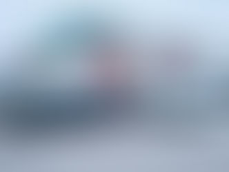 Green truck towing a gray camper with "alto" text, parked outside a building with "Safari Condo" sign. Overcast sky.