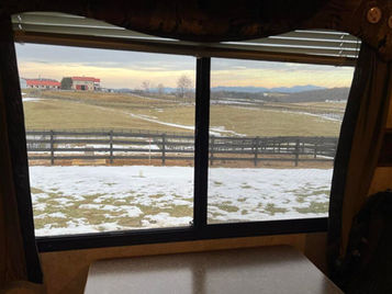 View of a snowy pasture with a fence with a barn in the distance.