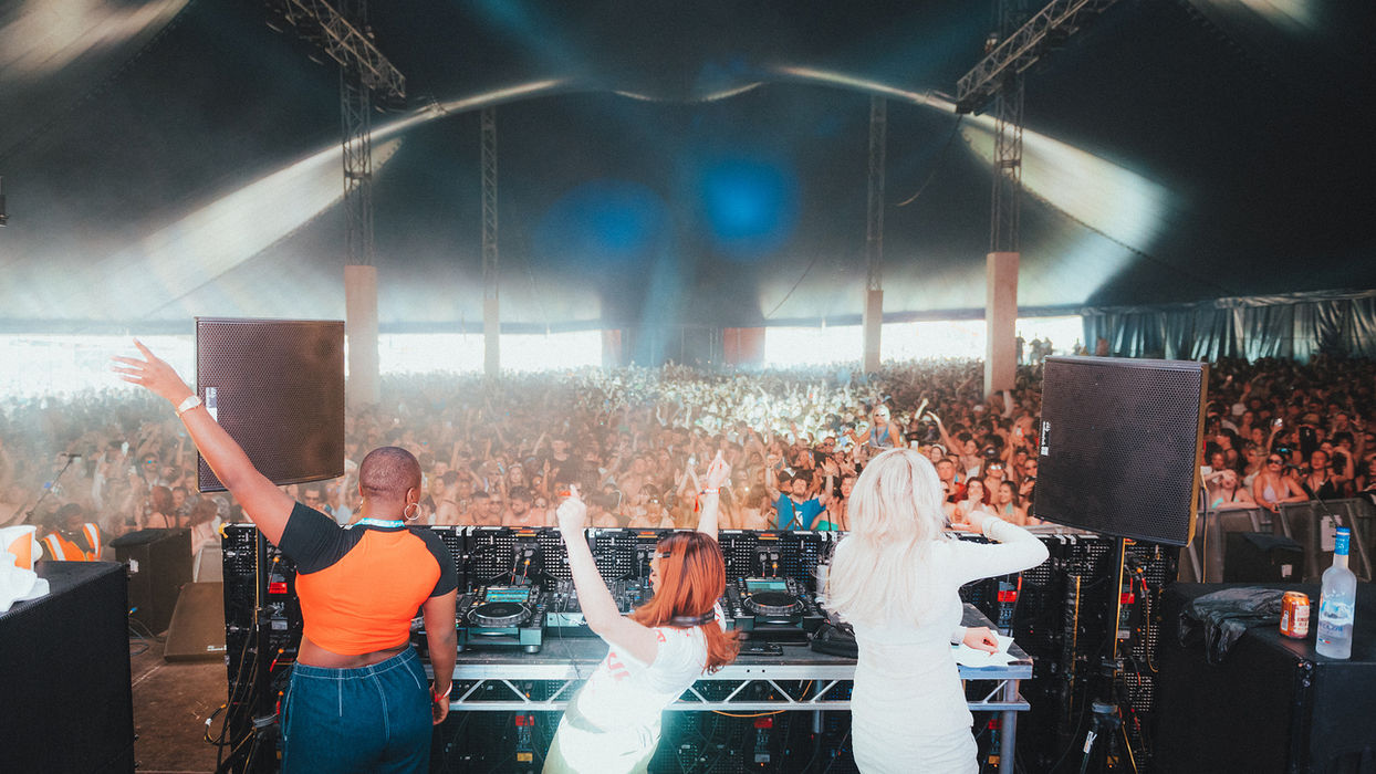 Girls Don't Sync DJ'in the Big Top stage. Performers stood behind the decks in front of a huge crowd in a covered Big Top stage.